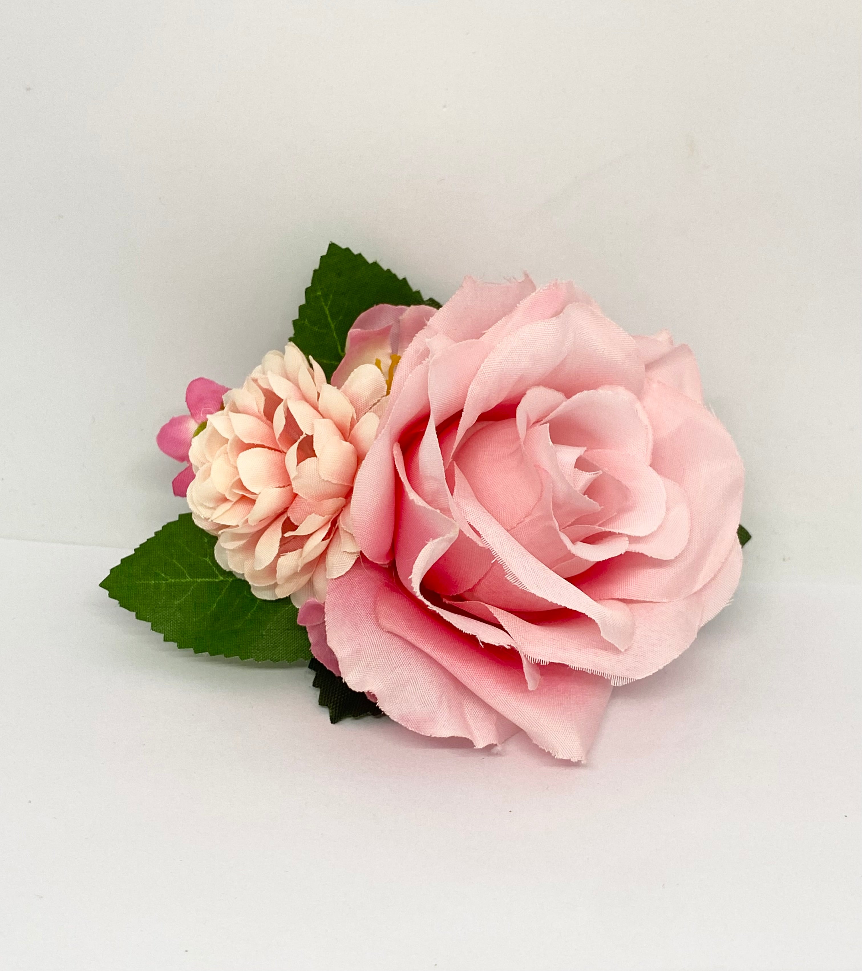 American Beauty A pink rose hair flower with a small green leaf attached, positioned against a white background. Pinup hair styling.
