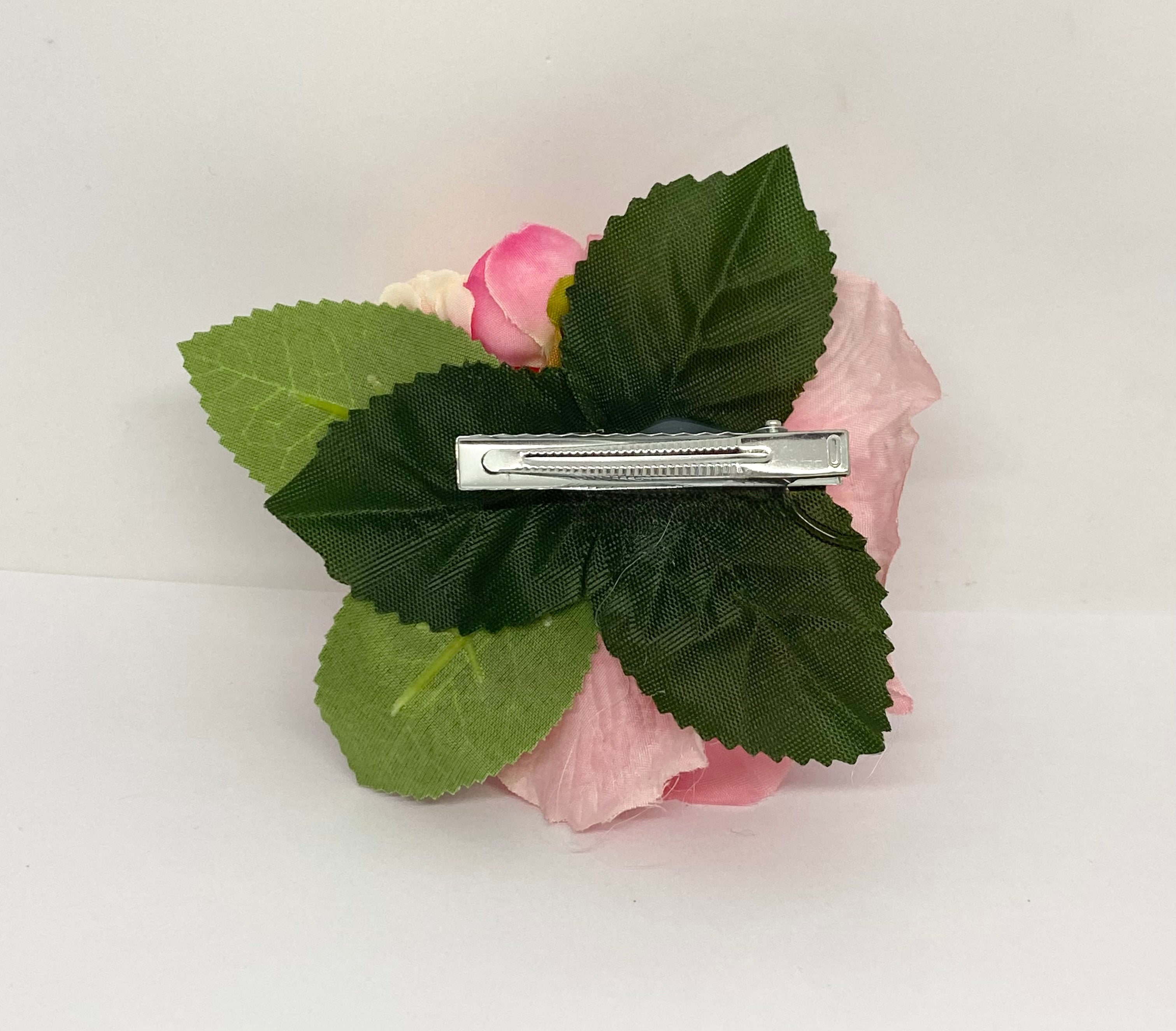 American Beauty A pink rose hair flower with a small green leaf attached, positioned against a white background. Pinup hair styling.