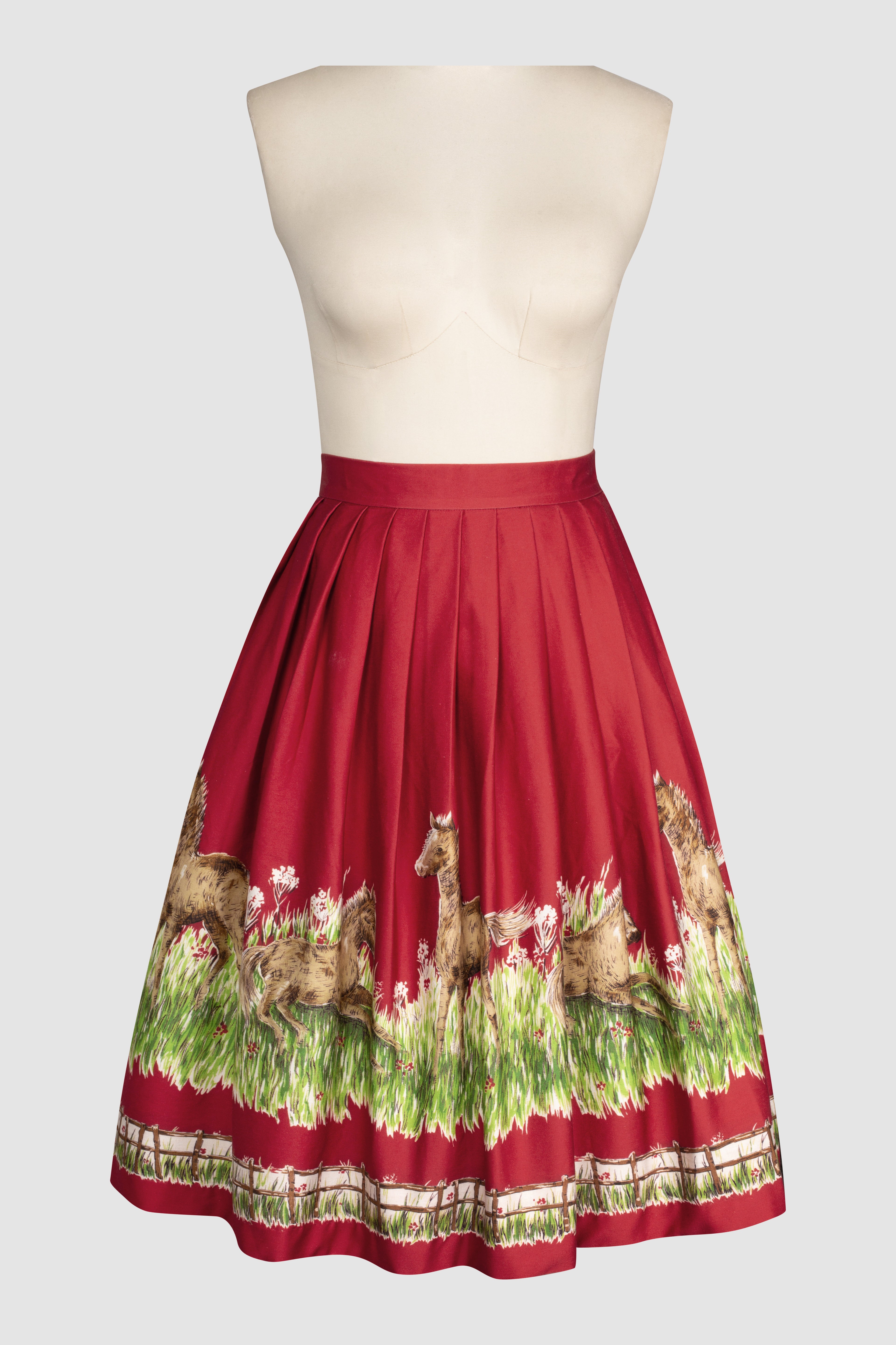 Corina 1950s style skirt with little pony’s in a green Pasture. Country novelty scene on a red background.