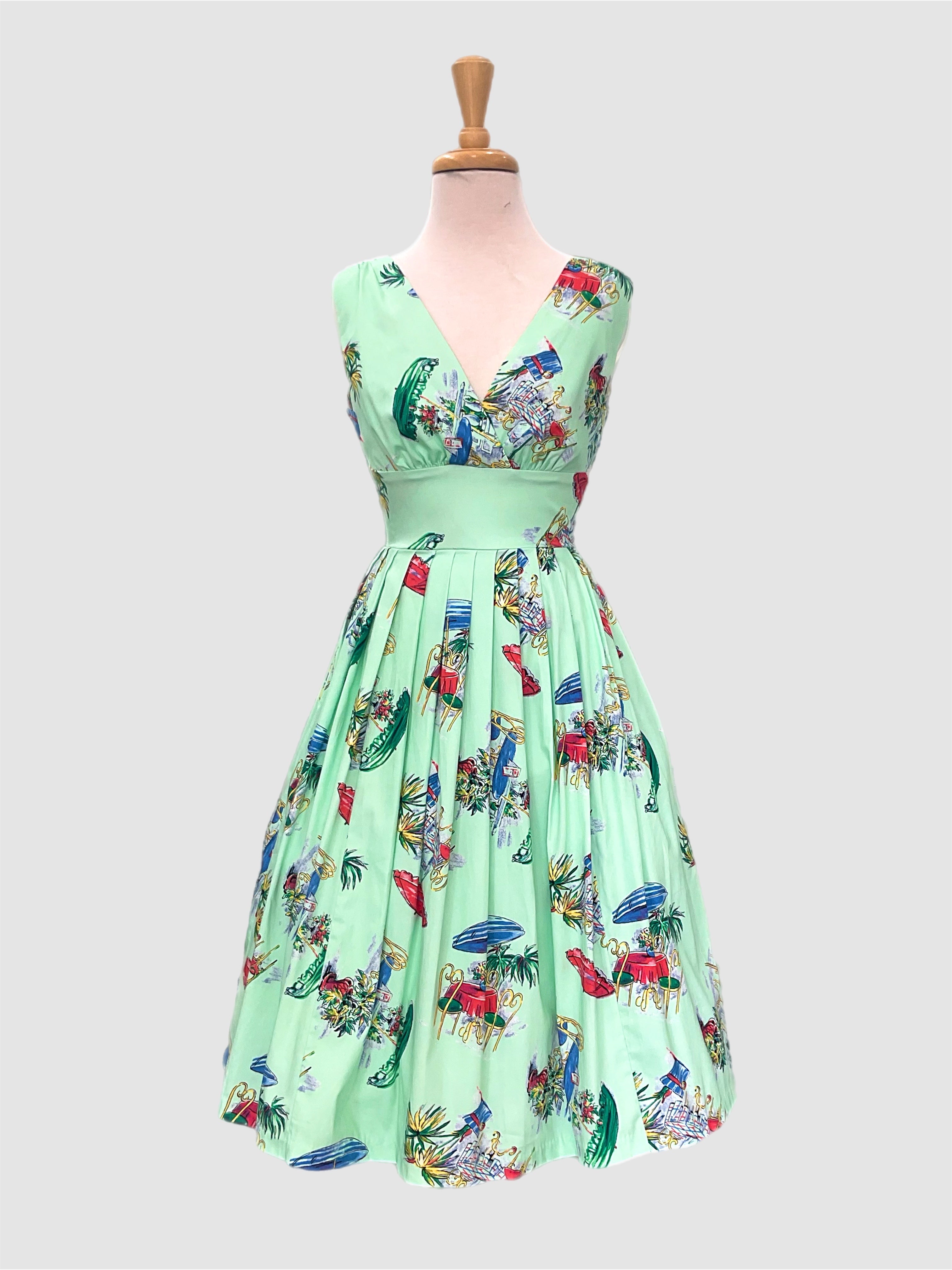  Vivian Le Parisian Cafe A vintage 1950's style dress with a green base and featuring a floral and Paris-themed novelty  print The dress has a V-neck, cap sleeves, and appears to be displayed on a mannequin.